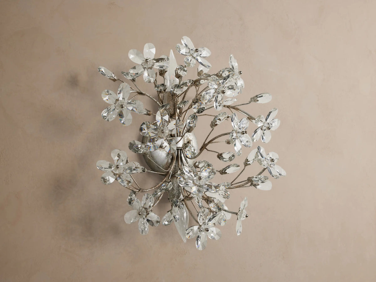 Antiqued silver Fiore Sconce, wall-mounted, featuring numerous clear crystal flowers & buds, with two lit candelabra bulbs.
