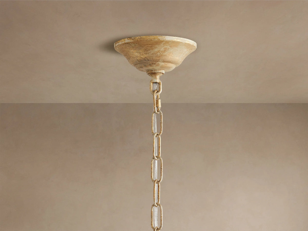 Close-up of Fiore Crown Chandelier's antiqued gold canopy & chain hanging from a light brown ceiling.