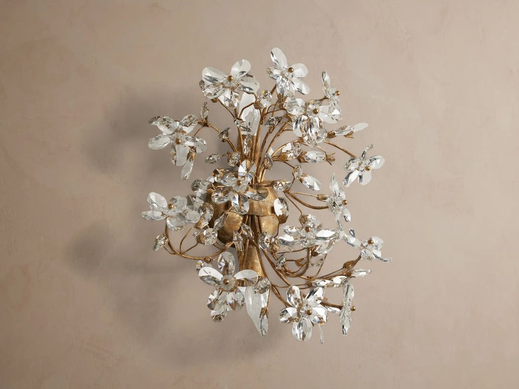 Fiore Sconce: Elegant gold iron sconce with clear crystal flowers, sparkling and glowing with warm light, mounted on a neutral wall.