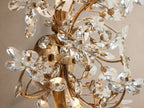Fiore Sconce: An antiqued gold wall fixture, a bouquet of clear crystal flowers and leaves, mounted on a light beige wall.