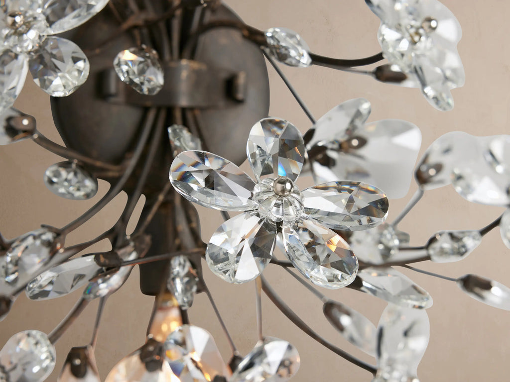 Fiore Sconce: Floral wall light with dark bronze branches and sparkling clear crystal flowers, mounted on a beige wall.