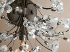 Fiore Sconce: Floral wall light with dark bronze branches and sparkling clear crystal flowers, mounted on a beige wall.
