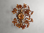 Fiore Sconce with a gold antiqued leaf design, featuring amber-colored flower-like structures radiating outward from a central base.