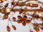 Fiore Linear Chandelier with intricate bronze leaf design, suspended by two gold chains and a central clear cord against a neutral background.
