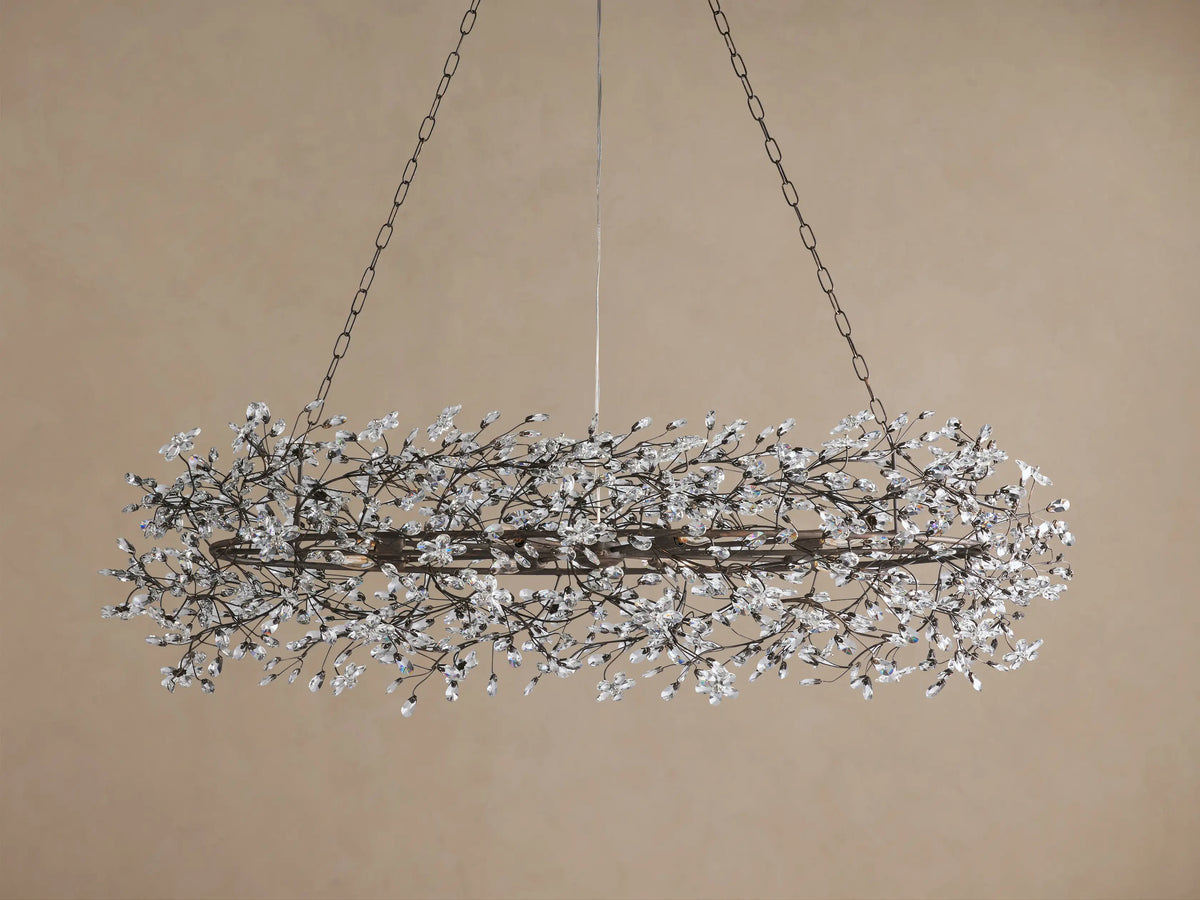 Fiore Oval Chandelier: horizontal oval dark metal frame with intricate branch-like design, adorned with numerous clear crystal blossoms, illuminated.