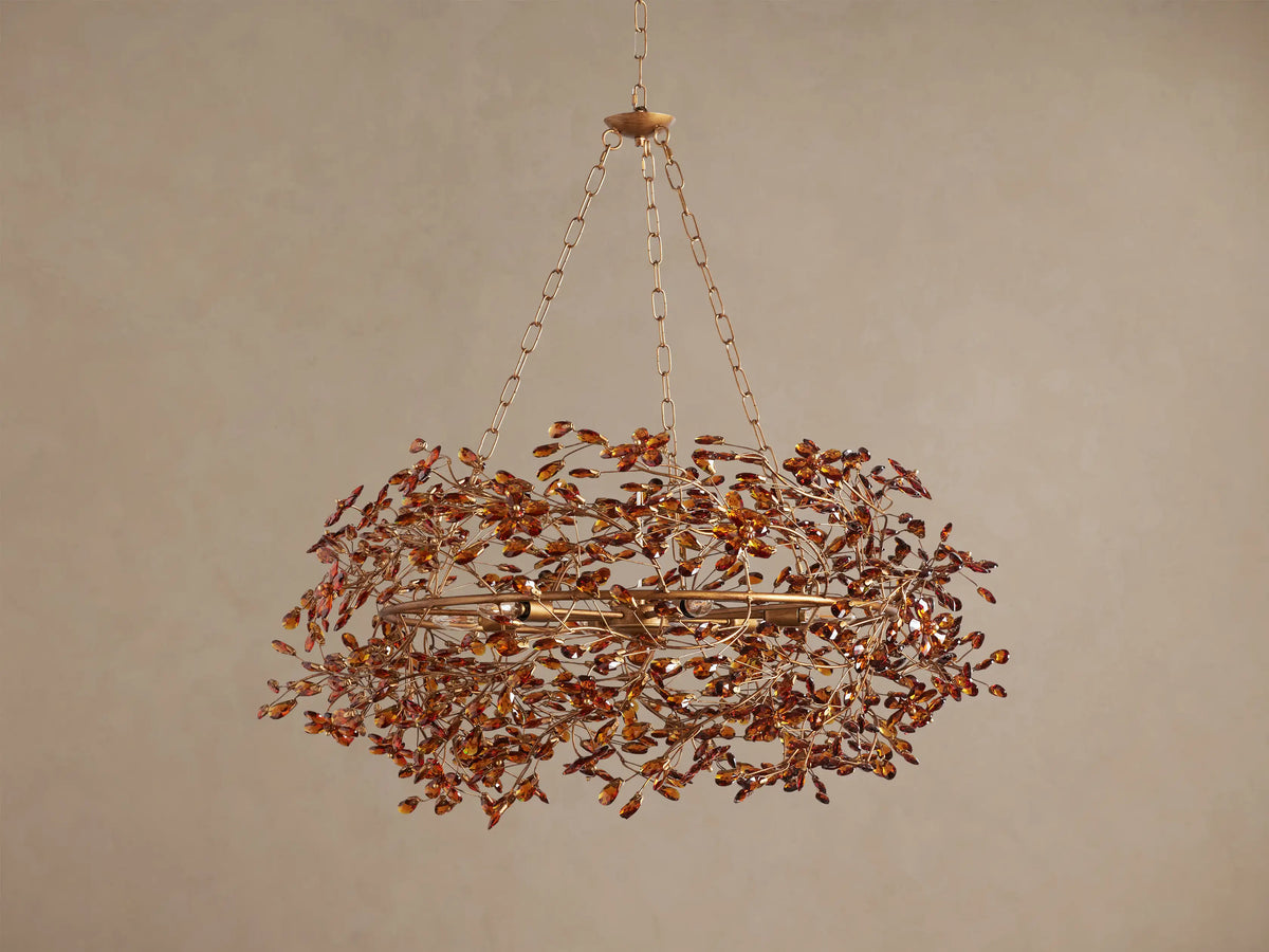Fiore Crown Chandelier: Gold-finished, circular chandelier adorned with numerous amber crystal leaves, hanging from a chain.