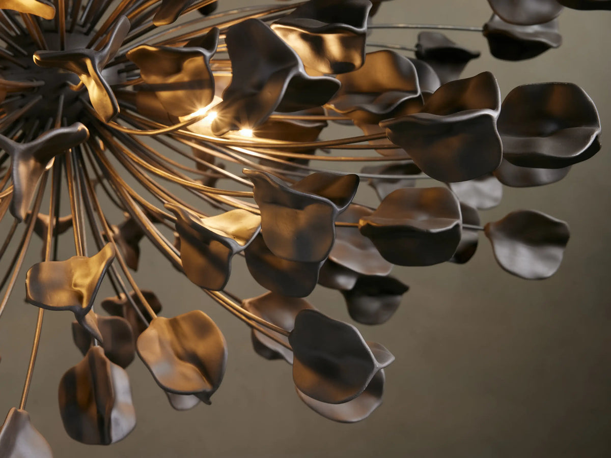 A dark iron chandelier with 160 ceramic leaves arranged in an organic, spherical design. Hangs from a chain against a beige wall.