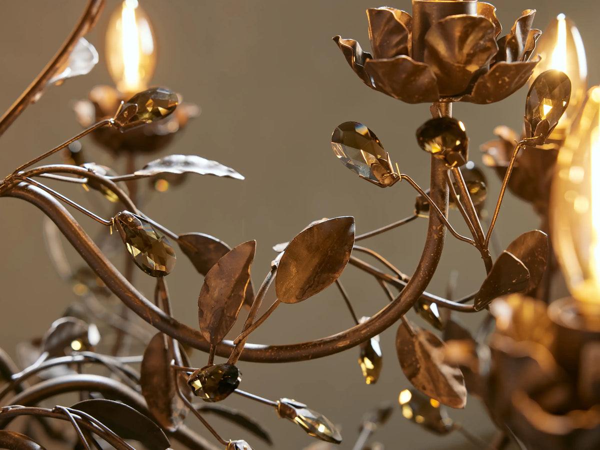 Nicoletta Round Chandelier close-up: ornate bronze iron with leaves, flower bulb holders, lit candelabra bulbs, smoke crystals.