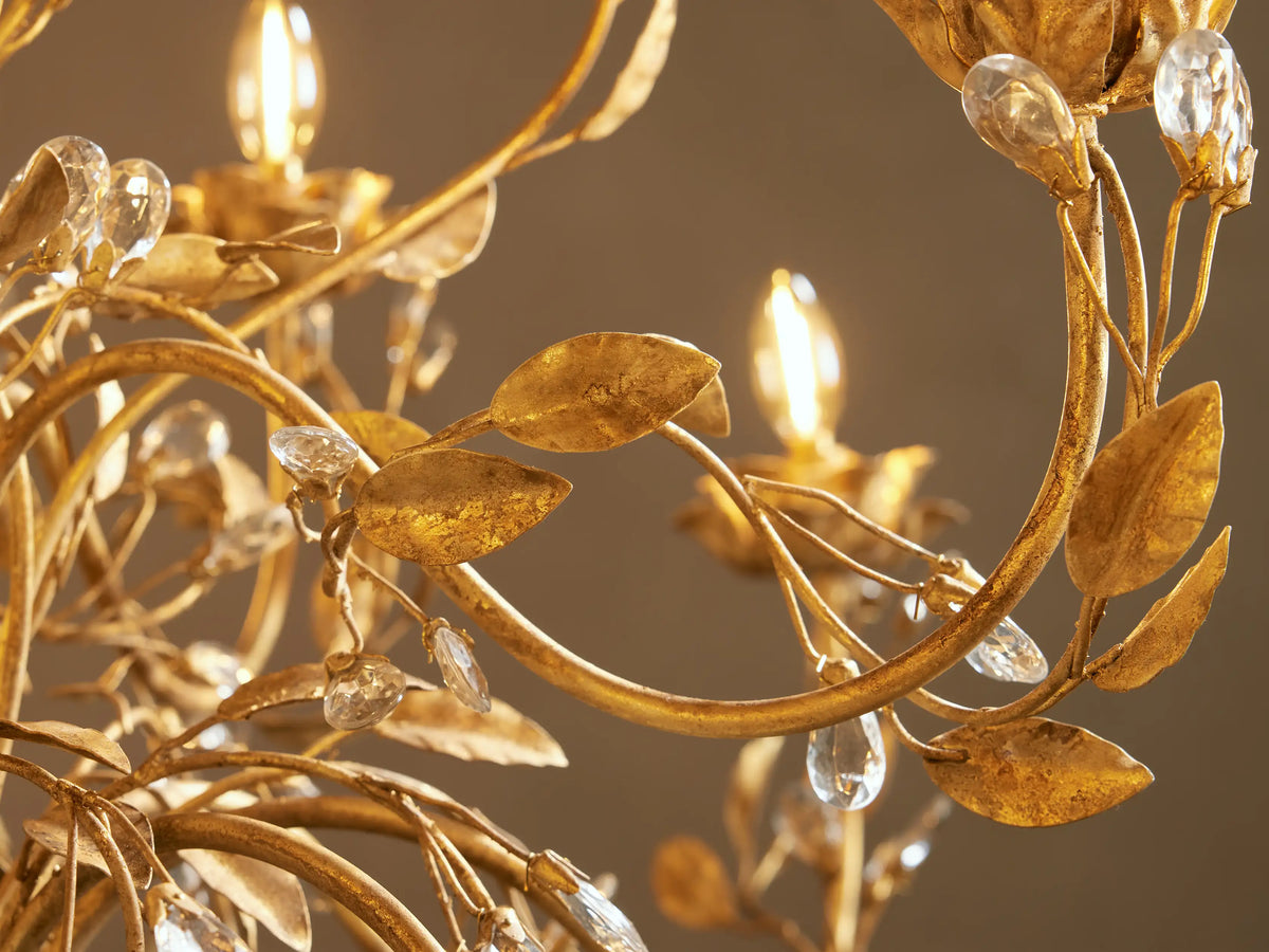 Close-up of a golden Nicoletta Round Chandelier with vine-like details, golden leaves, clear crystals, and glowing candle bulbs.