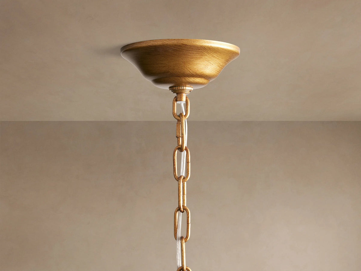 Close-up of the Ninfea Chandelier, showing detailed antiqued gold metal leaves and curved arms against a muted background.