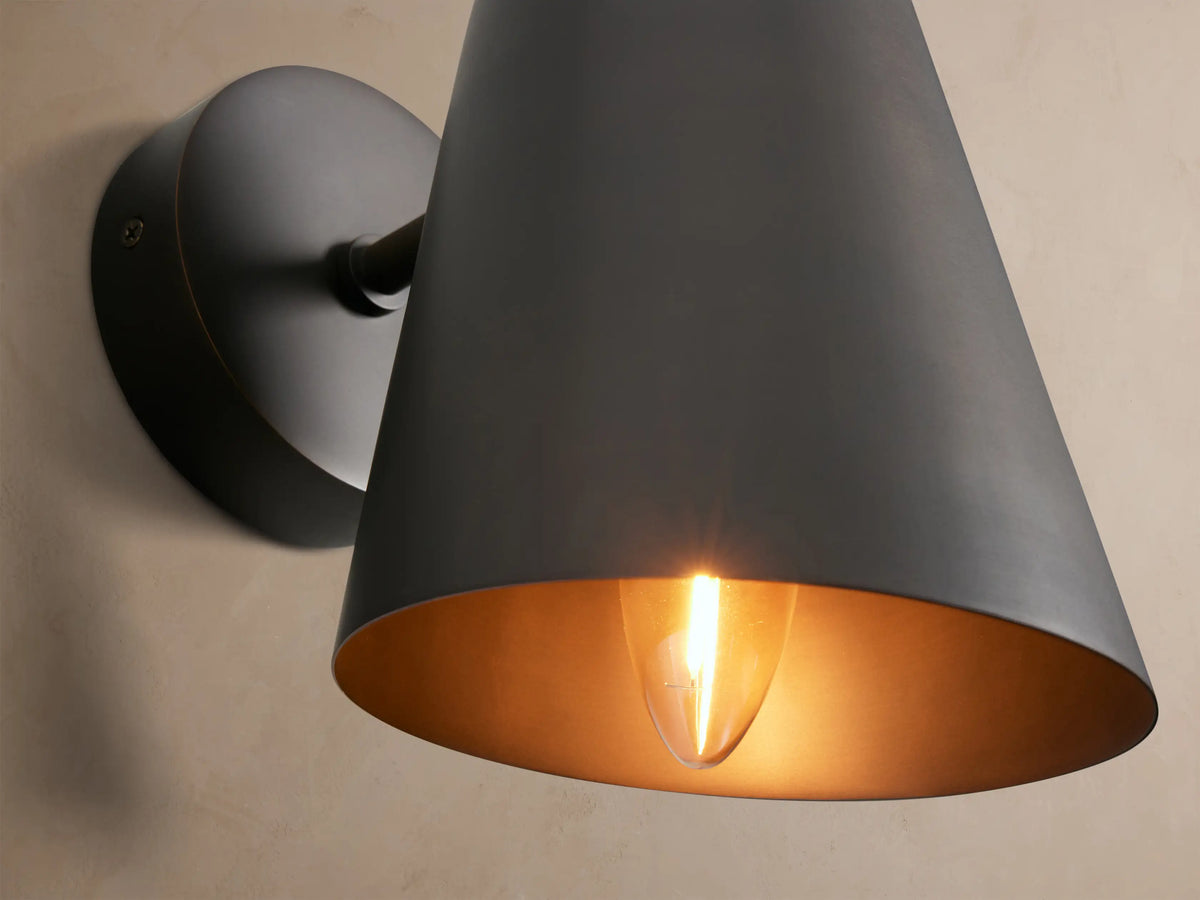 Elih Sconce in antiqued bronze finish, a wall-mounted light with a round backplate and downward-angled conical shade.