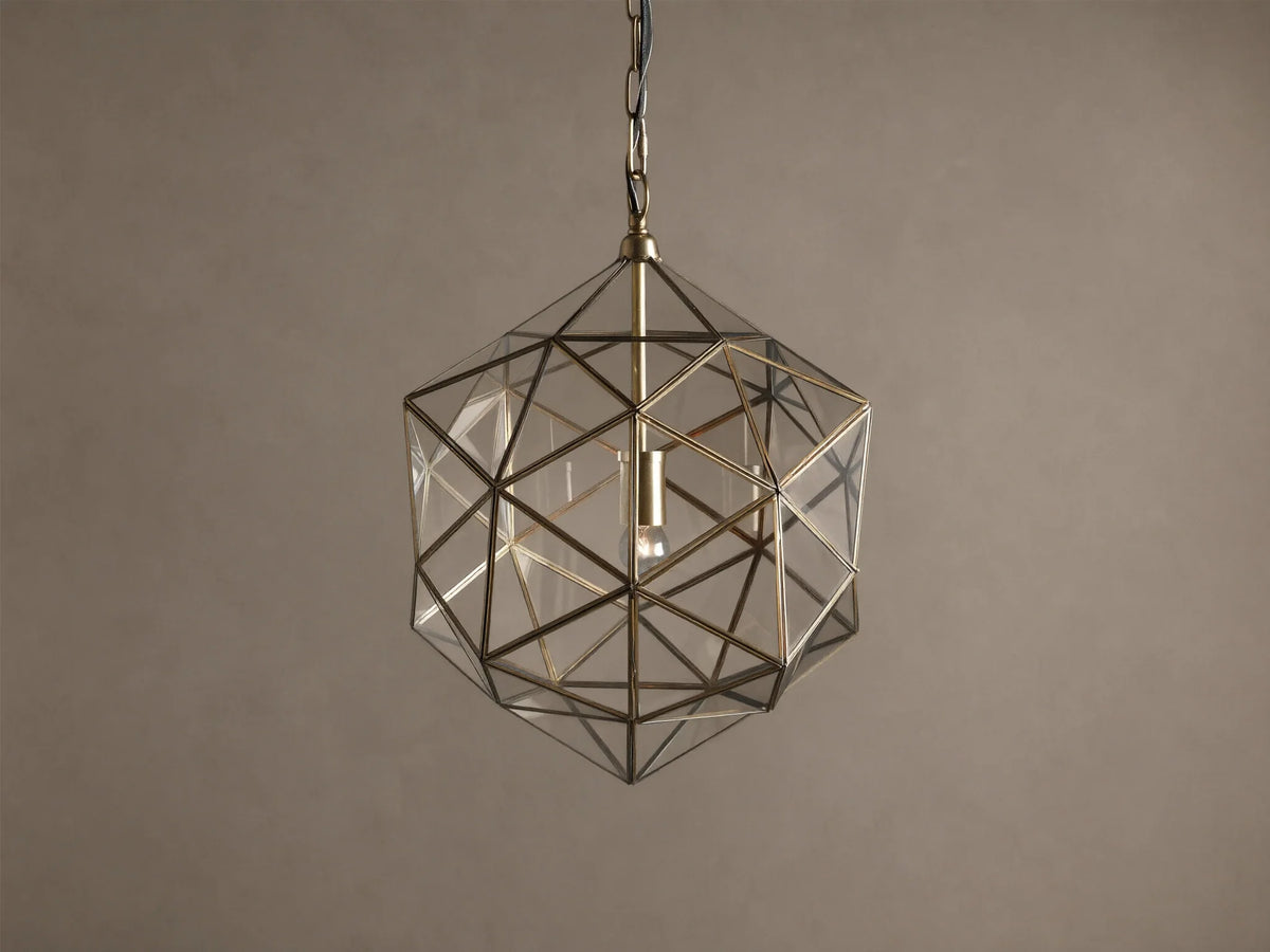 Eliana Lantern Pendant: Geometric brass and clear glass lantern hanging from a black chain, with a light bulb inside.