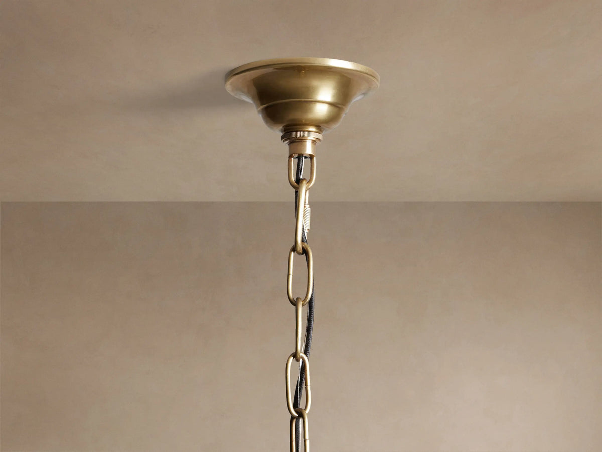 Eliana Lantern Pendant: Geometric brass and clear glass lantern hanging from a black chain, with a light bulb inside.