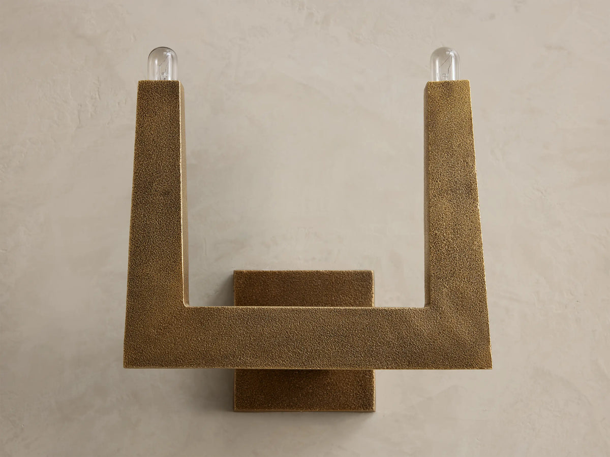 Front view of textured bronze U-shaped wall sconce with two glowing bulbs.