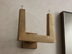 Golden textured wall sconce with an L-shaped arm and a lit bulb at the top, casting warm light on the wall.