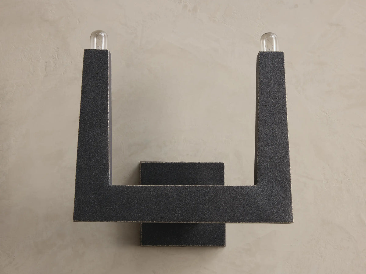 Front view of a dark gray textured U-shaped wall sconce with two upward-pointing clear bulbs.