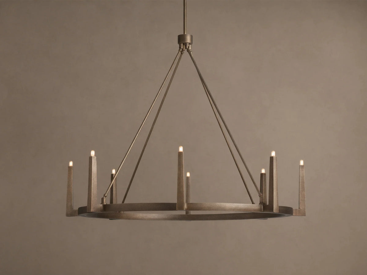 Emmet Round Chandelier in antiqued brass, with 8 illuminated candle-like lights on a circular frame, suspended from above.