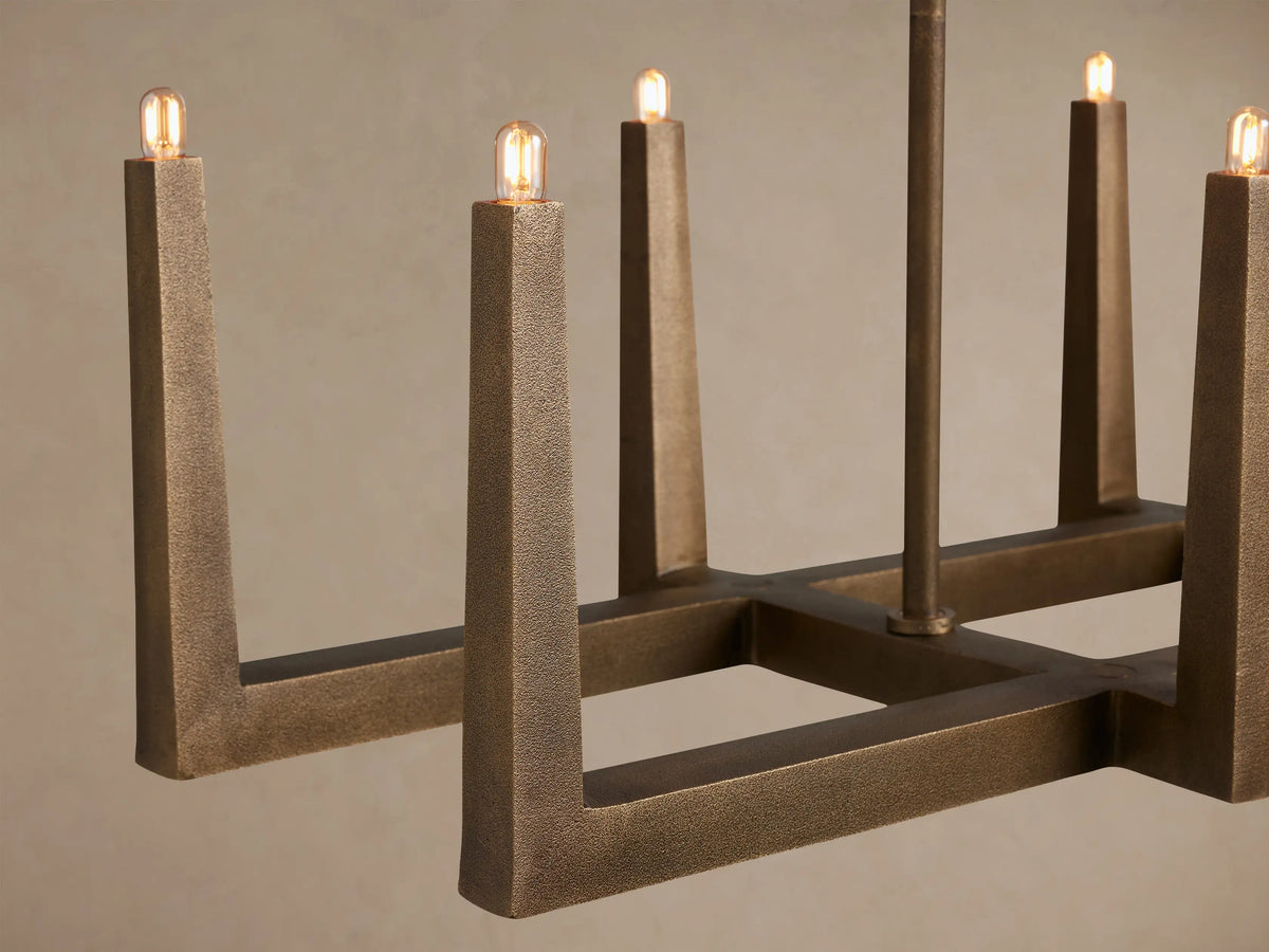 Emmet Linear Chandelier: Rectangular antiqued brass fixture with textured vertical arms holding small bulbs, suspended from above.
