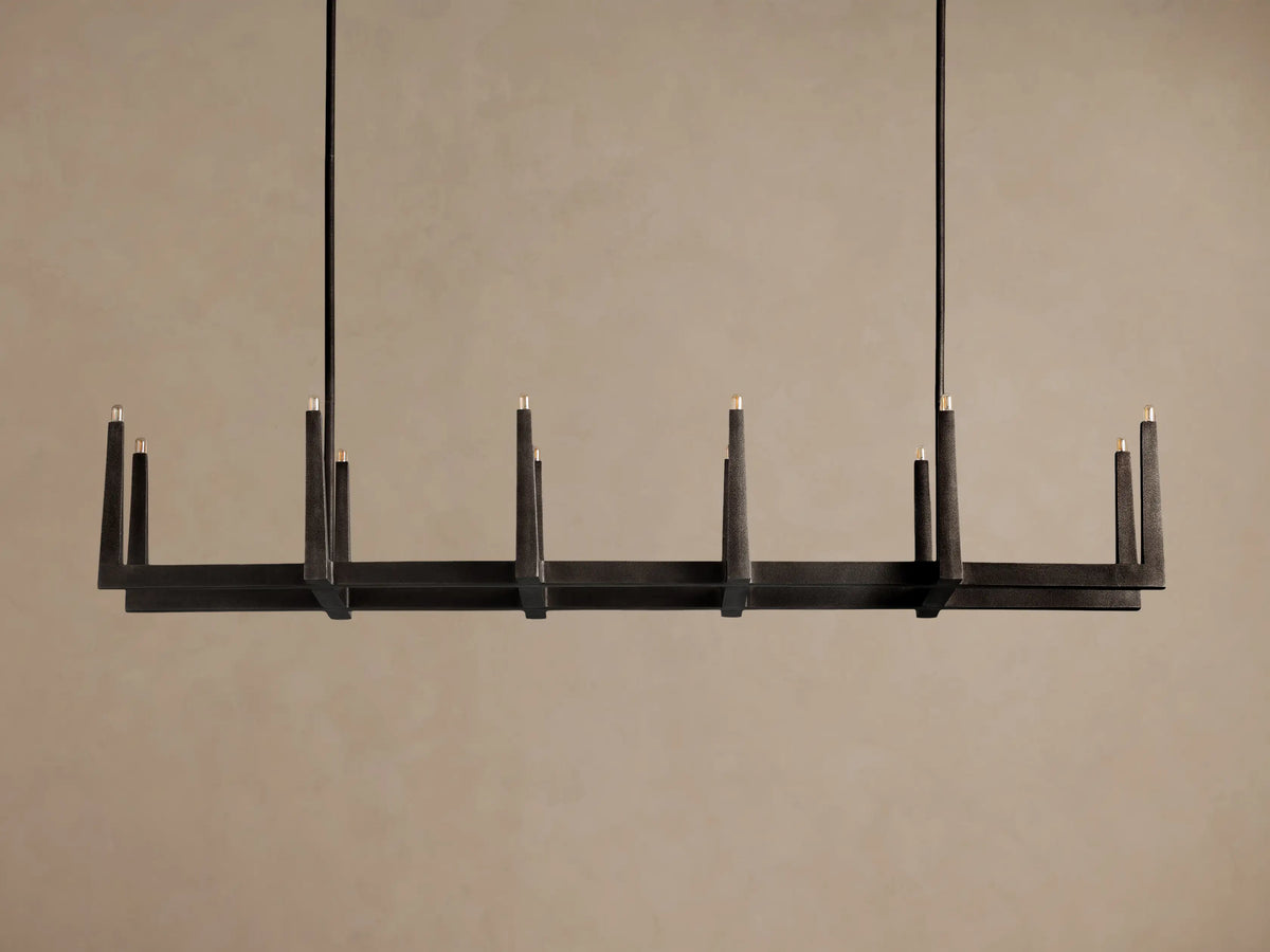 Emmet Linear Chandelier, dark antiqued textural brass, rectangular frame, 8 glowing candle-like lights on dark background.