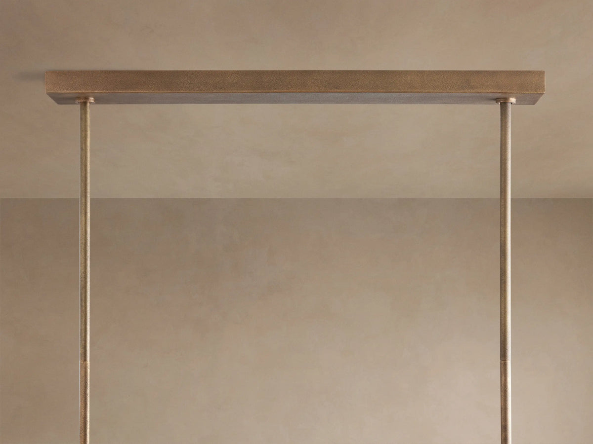 Close-up of Emmet Linear Chandelier. Antiqued brass, sand-casted frame with vertical arms and illuminated bulbs.