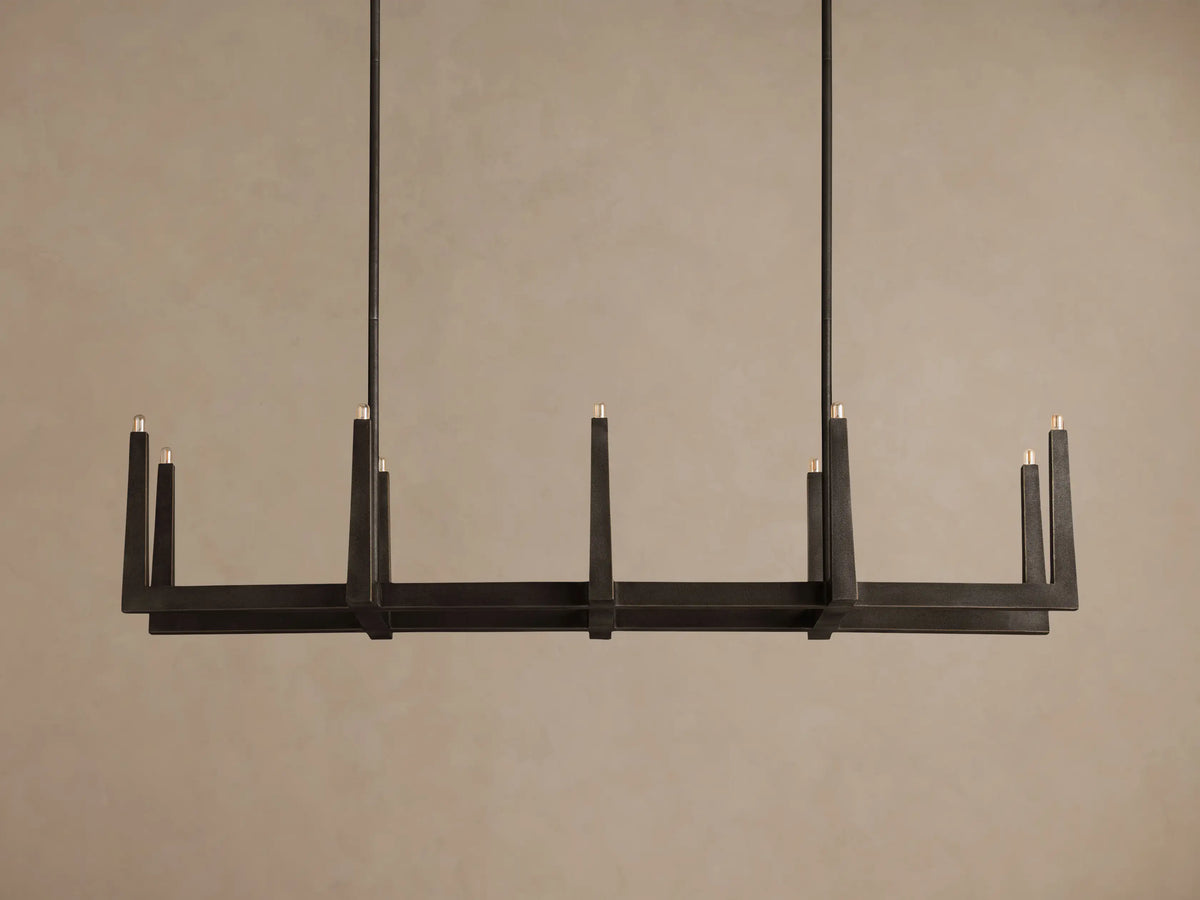 Emmet Linear Chandelier, dark antiqued brass linear fixture hung horizontally, showcasing ten lit candle-style bulbs.