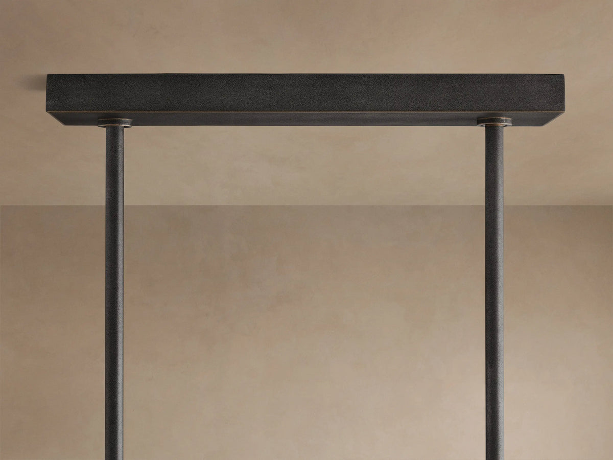 Emmet Linear Chandelier, dark textured antiqued brass frame with square arms, glowing filament bulbs visible.