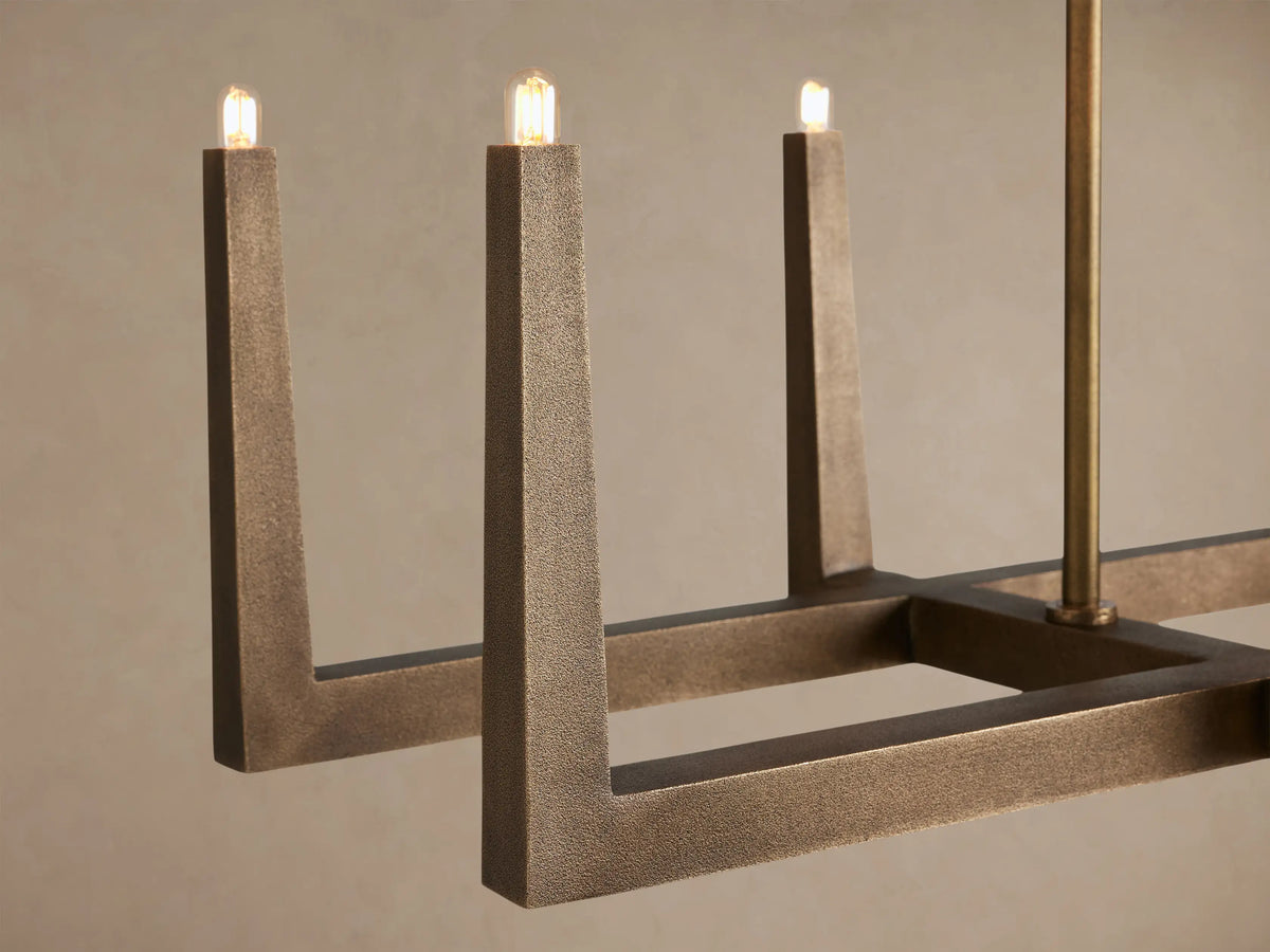 Emmet Linear Chandelier, antiqued brass linear frame with upward-facing light sockets, suspended from two rods against a plain wall.