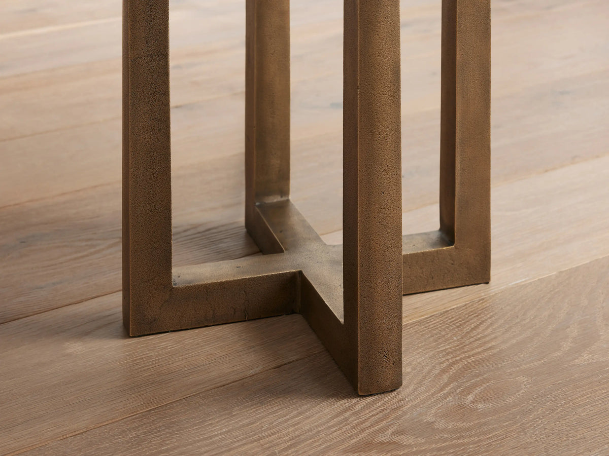 Close-up of Emmet Floor Lamp's antiqued bronze cast brass base with textured finish, forming a geometric cross on a light wood floor.