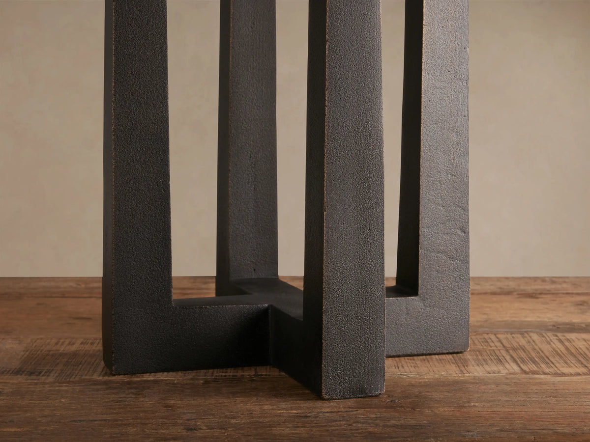 Emmet Table Lamp with white linen shade and dark, textured antiqued brass three-pillar base on a rustic wooden table.