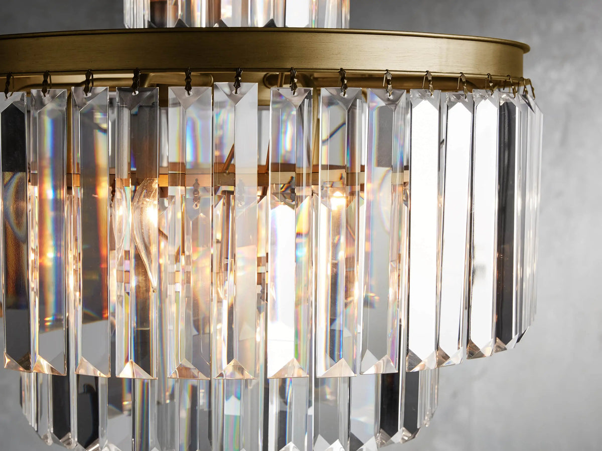 Leyland Chandelier with multifaceted K9 glass crystals, gold iron frame, and layered design, hanging from a chain against a gray background.