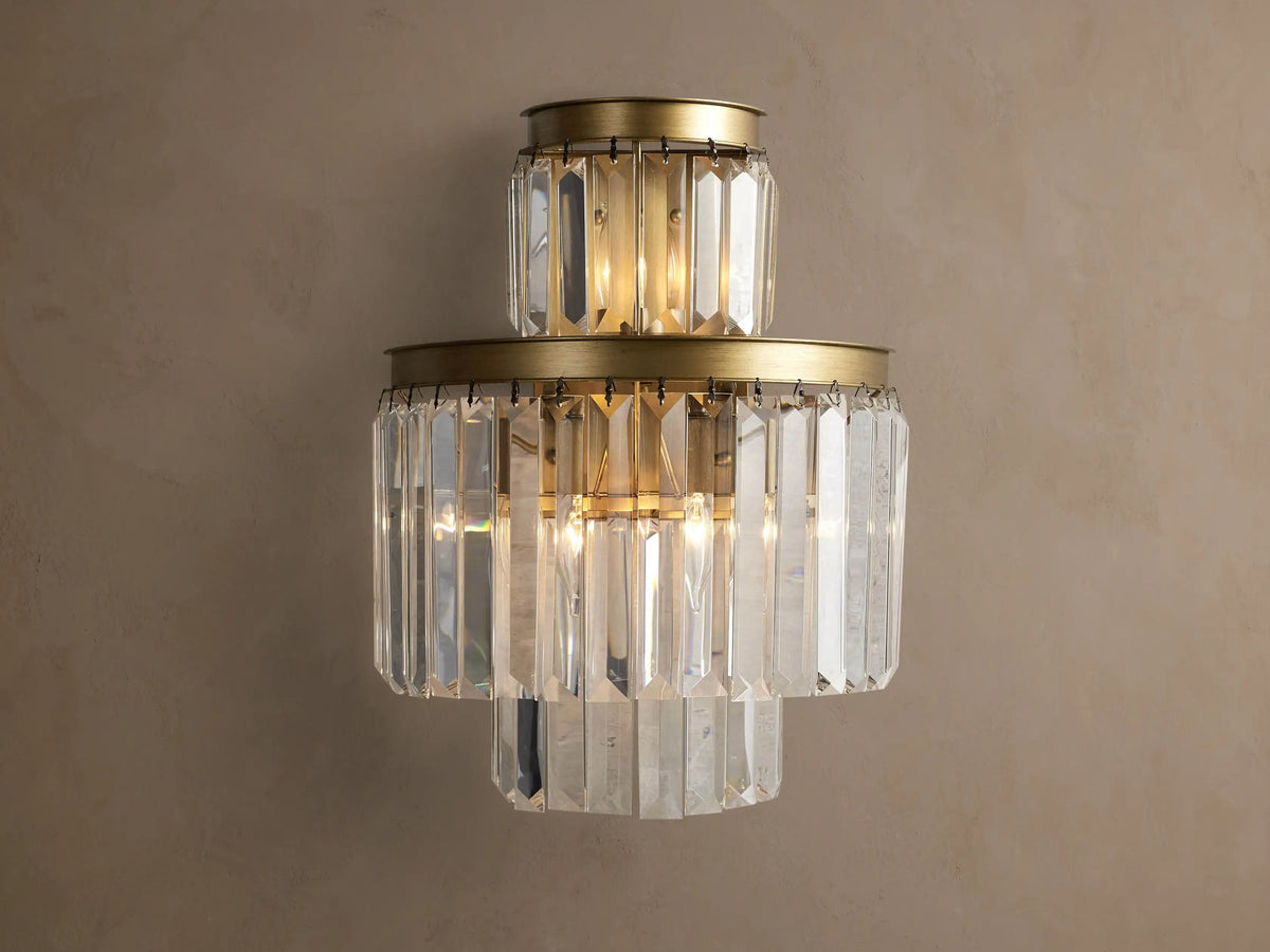 Leyland Sconce: a tiered wall light with illuminated clear K9 glass crystals & an oil-rubbed bronze-toned frame against a wall.