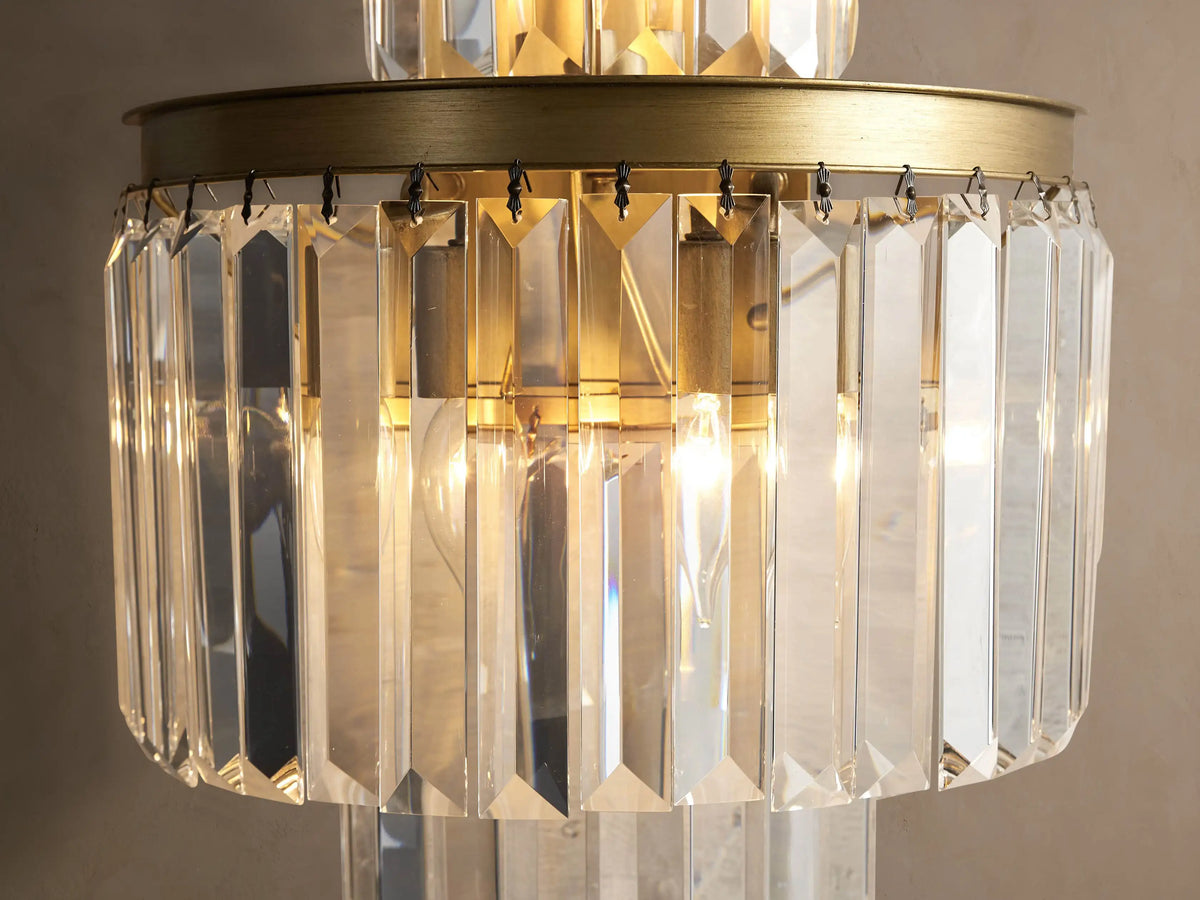 Leyland Sconce: a tiered wall light with illuminated clear K9 glass crystals & an oil-rubbed bronze-toned frame against a wall.