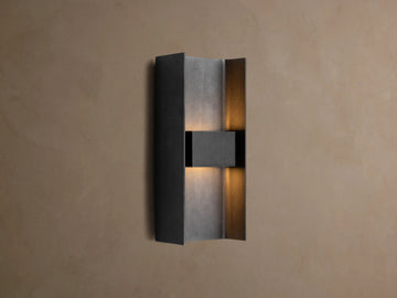 Sidney Outdoor Sconce, a graphite aluminum fixture casting warm LED light up and down against a taupe wall.