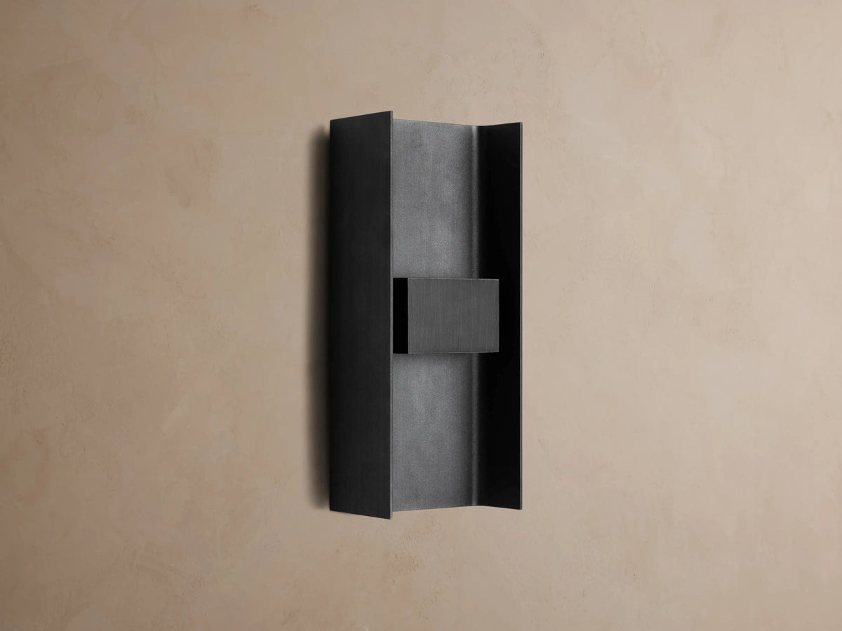 Sidney Outdoor Sconce, a graphite aluminum fixture casting warm LED light up and down against a taupe wall.