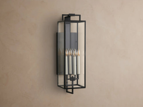 Hendricks Outdoor Sconce: black iron frame with clear glass panels, four lit candle-style bulbs, mounted vertically on a taupe wall.