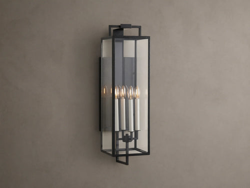 Hendricks Outdoor Sconce: black iron frame with clear glass panels, four lit candle-style bulbs, mounted vertically on a taupe wall.