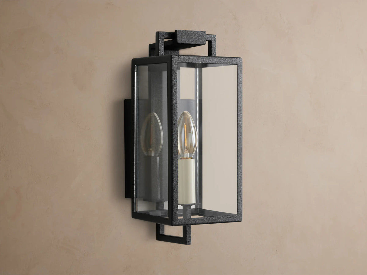 Hendricks Outdoor Sconce: black iron rectangular lantern, clear glass, two candle-style bulbs, mounted on a taupe wall.