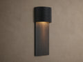 Fultz Outdoor Sconce, a soft black wall-mounted fixture with a horizontally ridged top and vertically ridged base, glowing warm light.