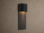 Fultz Outdoor Sconce, a soft black wall-mounted fixture with a horizontally ridged top and vertically ridged base, glowing warm light.
