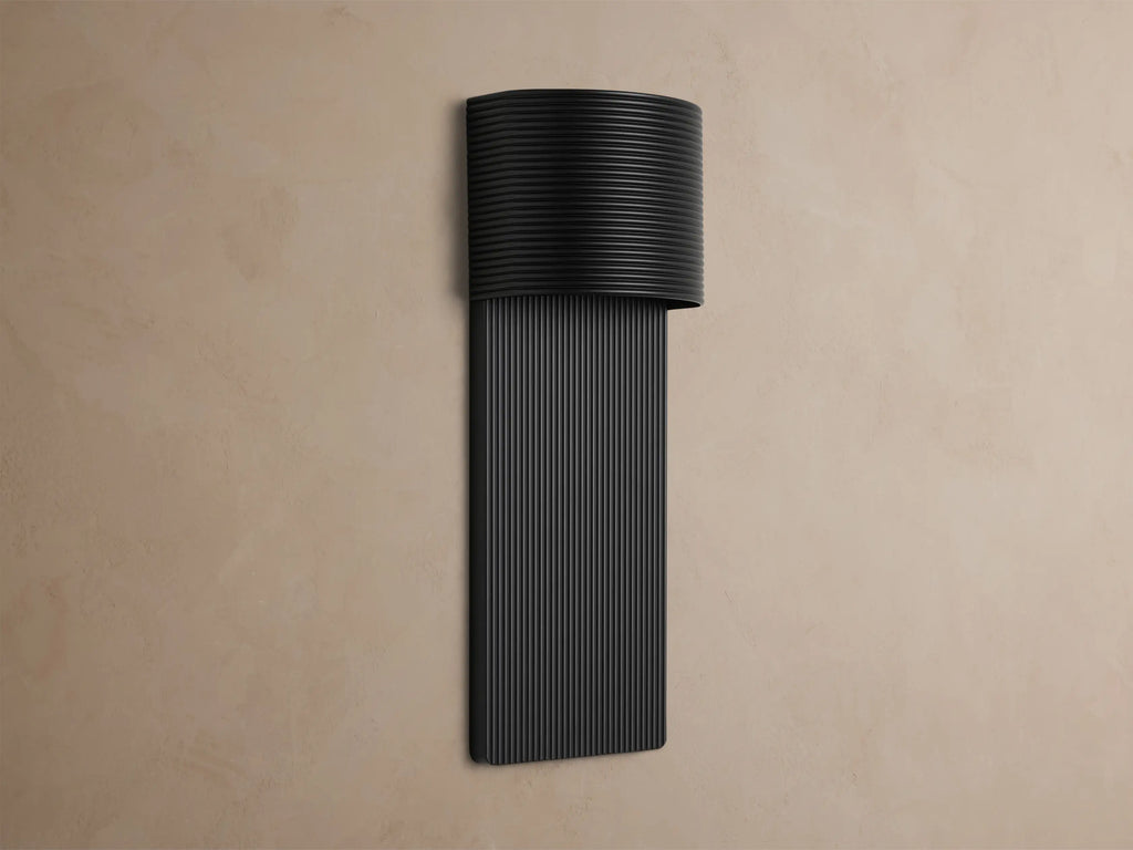 Fultz Outdoor Sconce, a soft black wall-mounted fixture with a horizontally ridged top and vertically ridged base, glowing warm light.