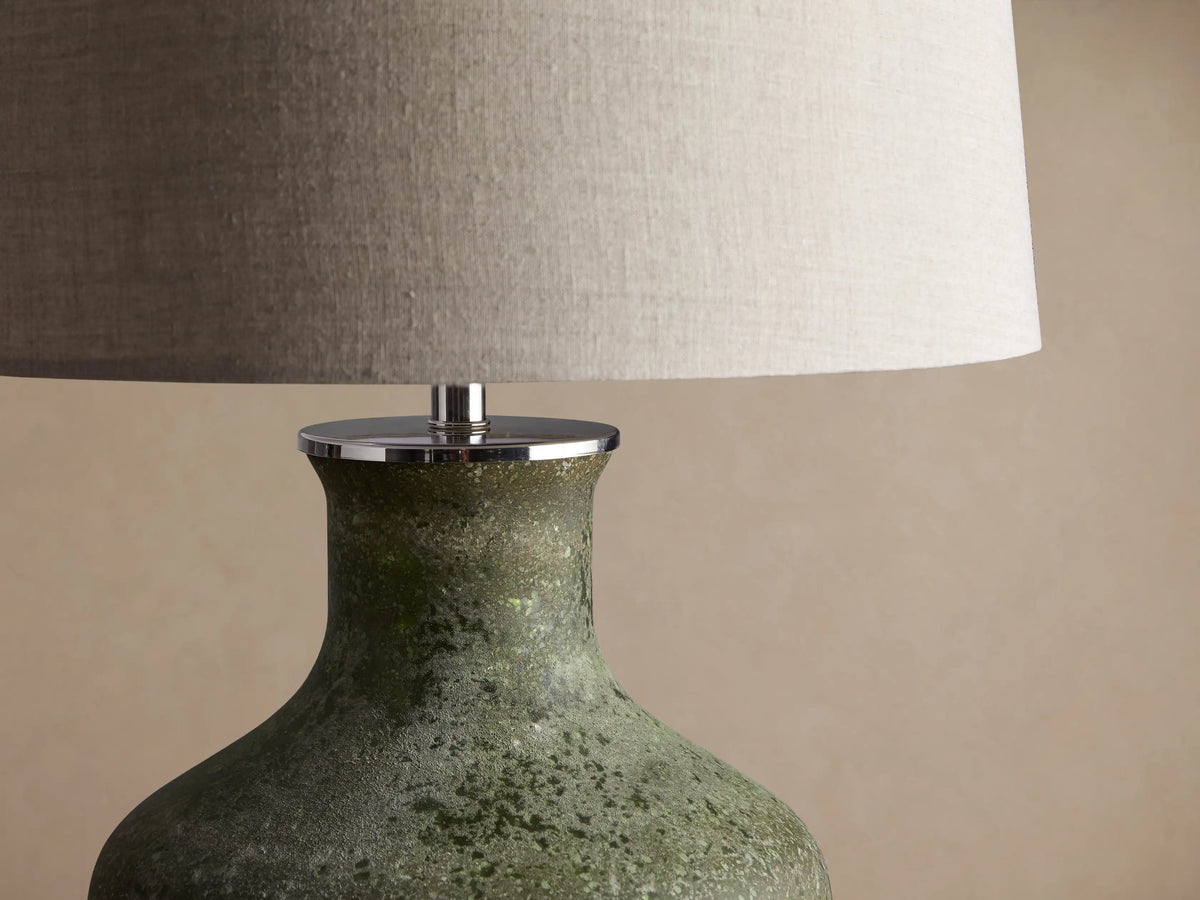 Galena Table Lamp: Green, sand-blasted glass bottle-shaped base with a light linen shade on a rustic wood surface.