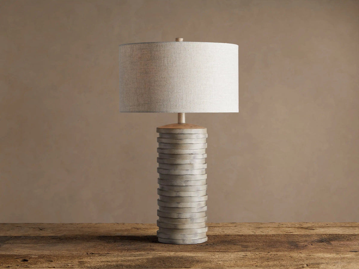 Maeve Taupe Table Lamp with a distressed stacked taupe cylindrical base & a light beige fabric drum shade.