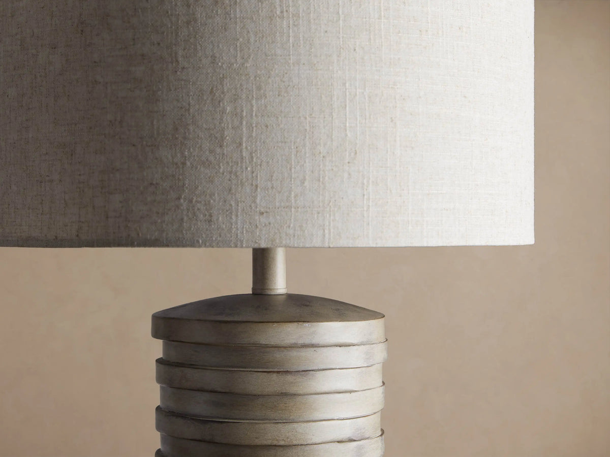 Maeve Taupe Table Lamp with a distressed stacked taupe cylindrical base & a light beige fabric drum shade.