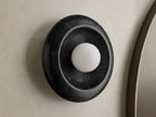 Front view of round black marble wall sconce with white spherical bulb, mounted on light wall next to wooden mirror frame.