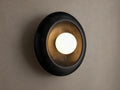 Close-up of a round black cracked marble wall sconce with a distressed gold interior and a glowing white spherical bulb.