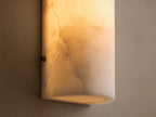 A cylindrical wall-mounted light fixture made of white marble with subtle grey veining, set against a beige wall.