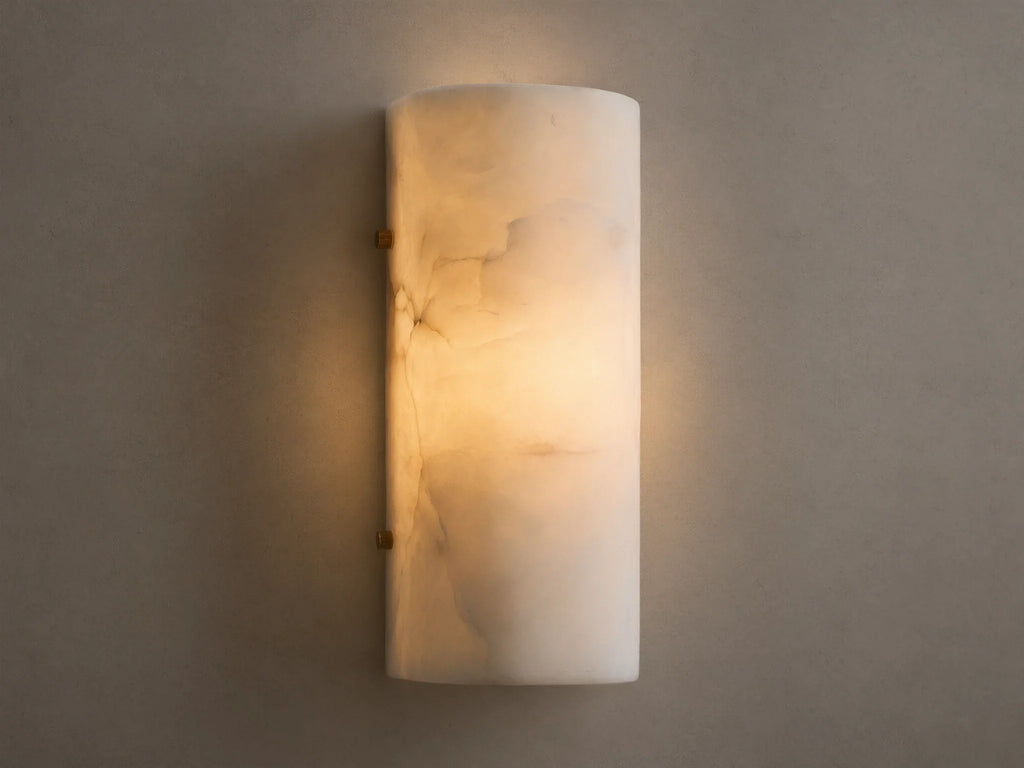 Wall-mounted cylindrical sconce made of alabaster, softly glowing with warm, inviting light against a beige textured wall.