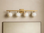 Arica Wall Sconce with four illuminated round glass shades mounted on a horizontal brass fixture above a mirror.