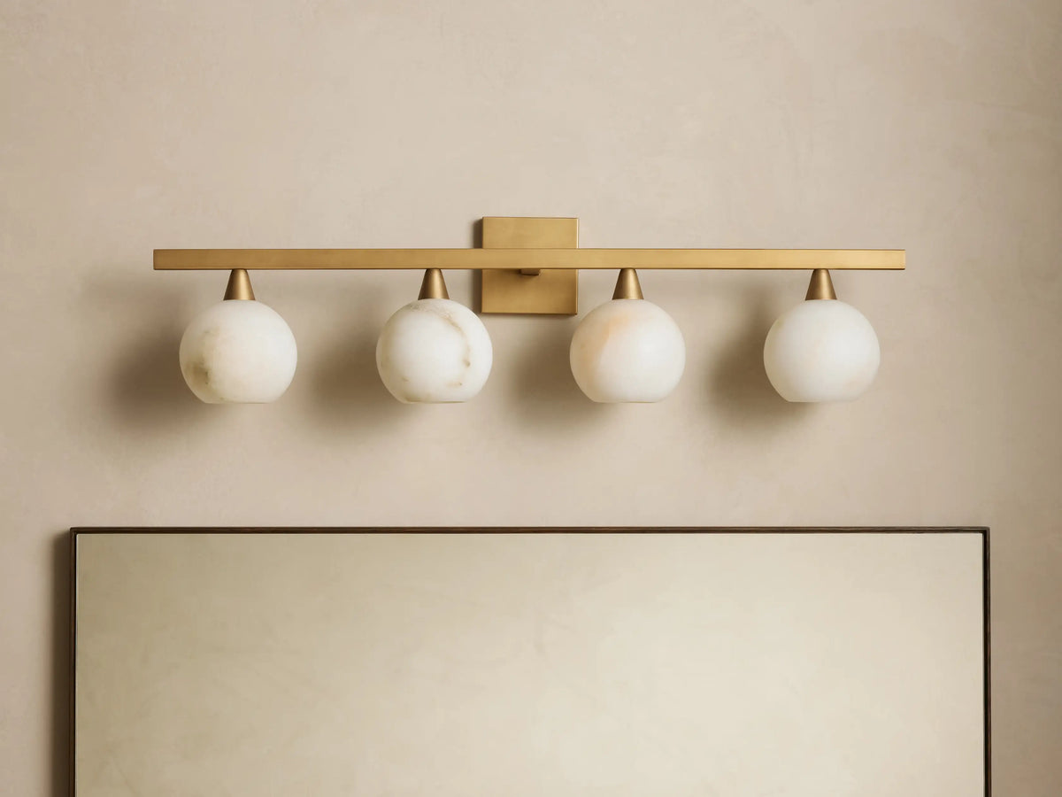 Arica Wall Sconce with four illuminated round glass shades mounted on a horizontal brass fixture above a mirror.