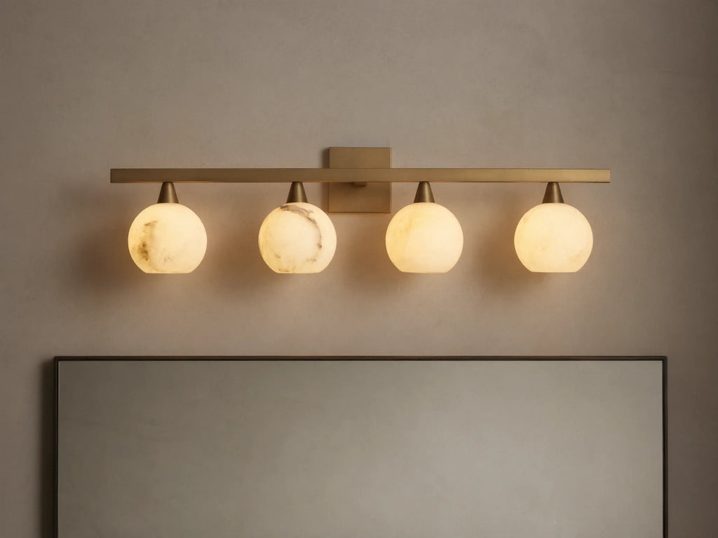 Arica Wall Sconce with four illuminated round glass shades mounted on a horizontal brass fixture above a mirror.
